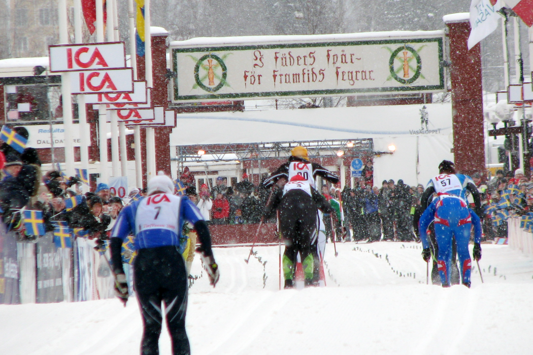 Skidåkare på upploppet i Vasaloppet. I bakgrunden syns Vasaloppets klassiska målportal med texten "i fäders spår för framtids segrar".