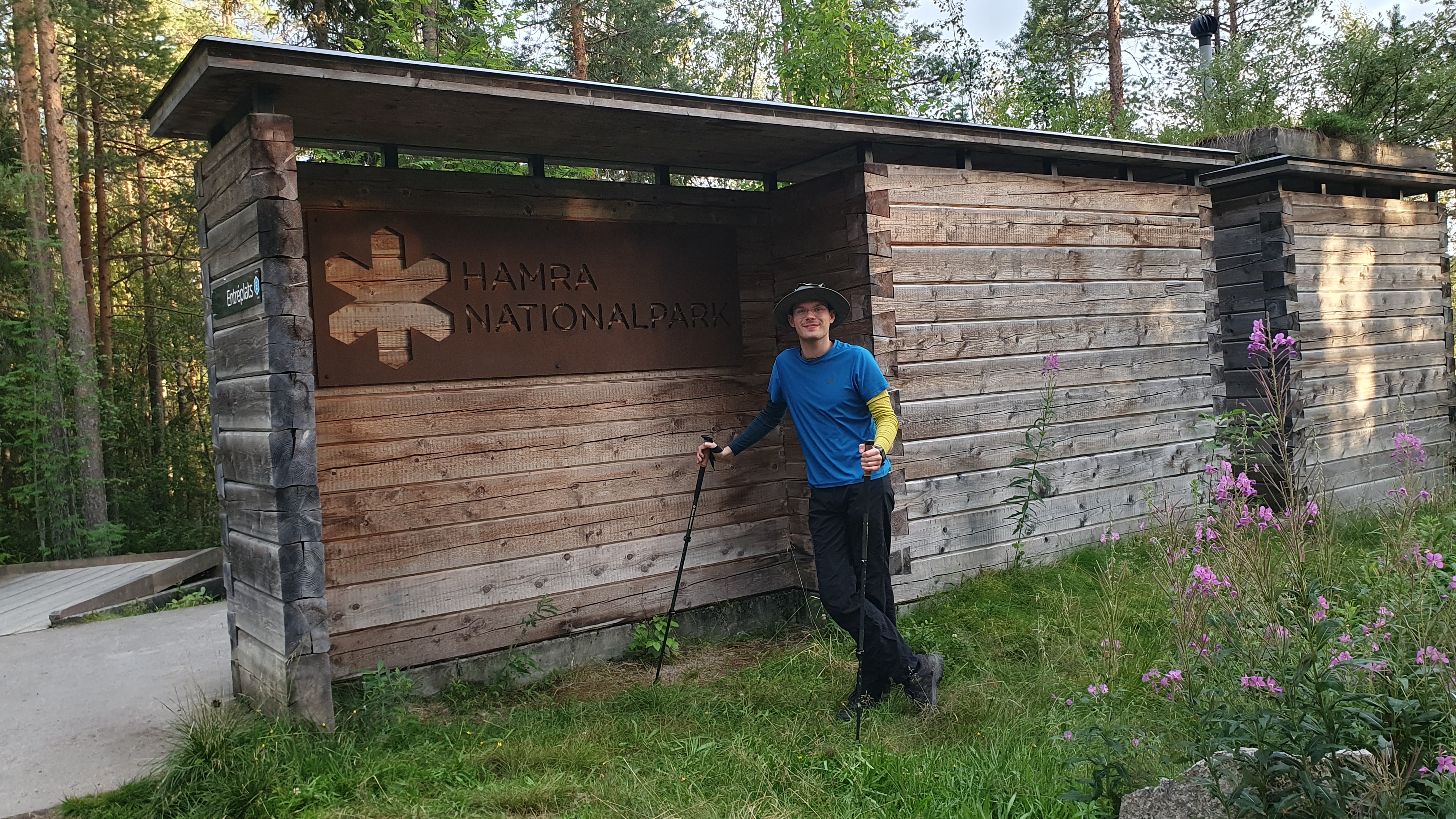 Student in blue t-shirt standing in front a wooden cabin