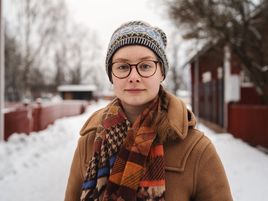 Kvinna i brun rock står utomhus, det ligger snö på backen.